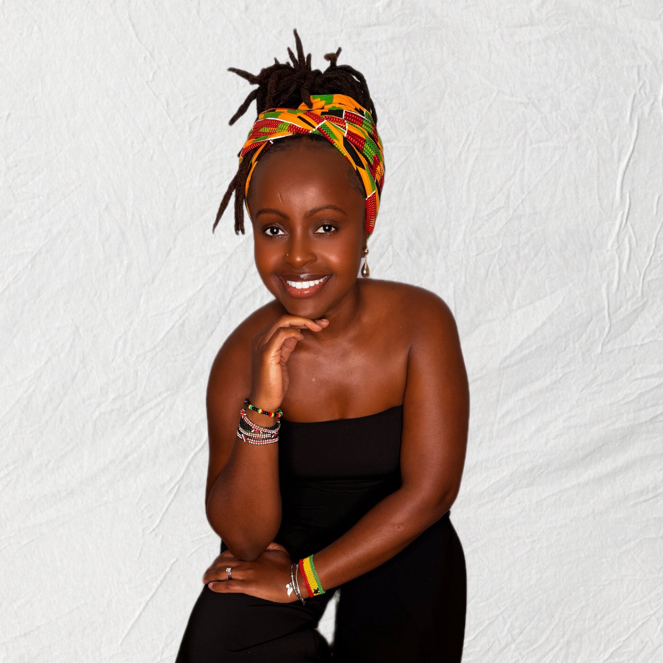 Woman wearing a black dress and colorful headscarf on a textured white background